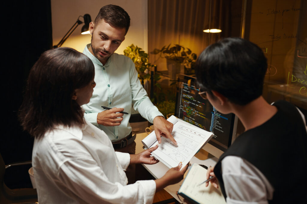 A group of developers collaborating on wireframe designs and code at a computer workstation, illustrating DevOps principles and Project Based Learning through active teamwork and interface planning.